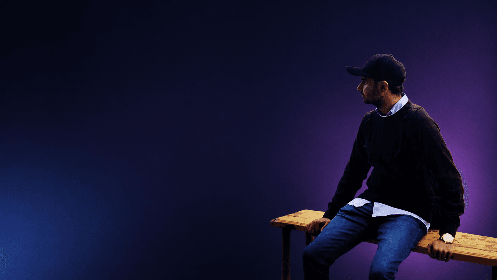Abdul Moiz Memon sitting on a bench against a blue and purple background